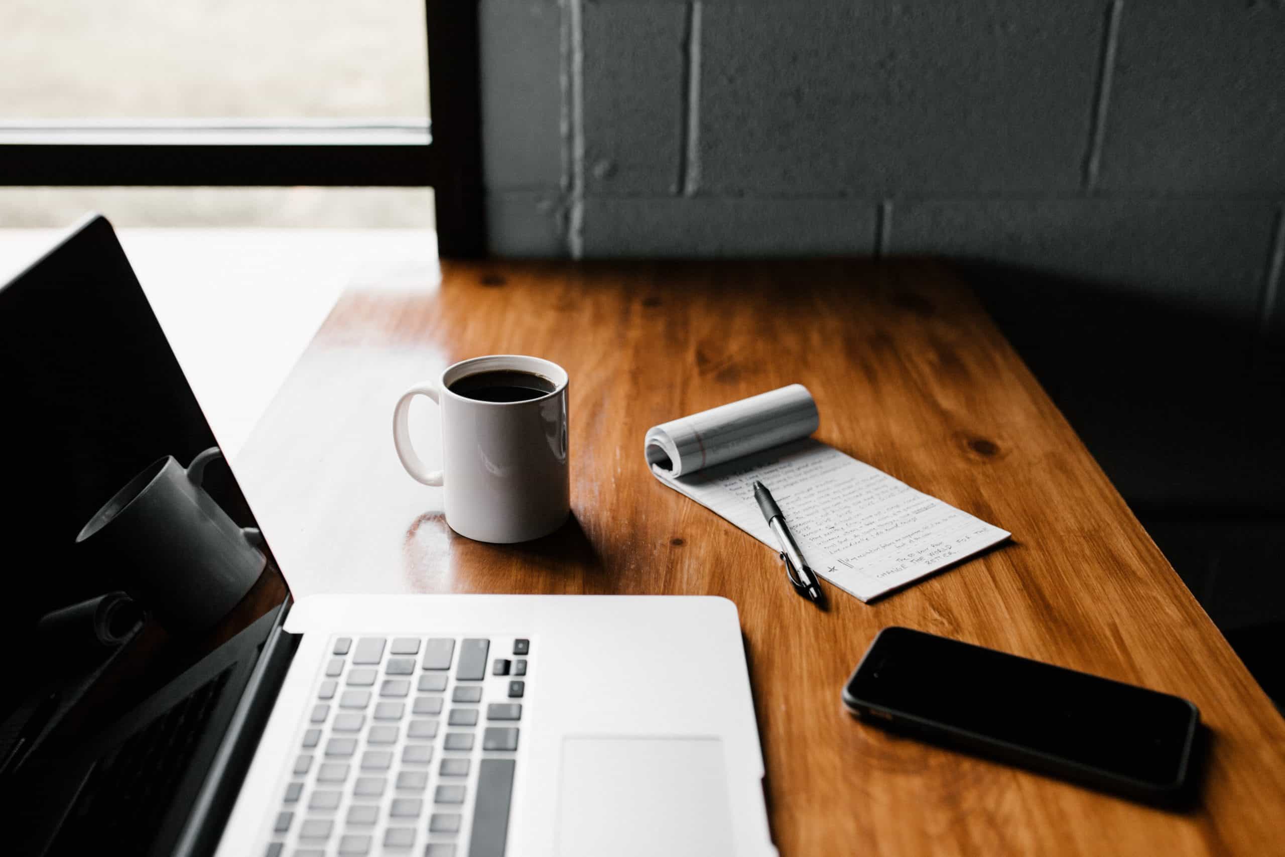 Laptop, Coffee mug and pad of paper on a desk.